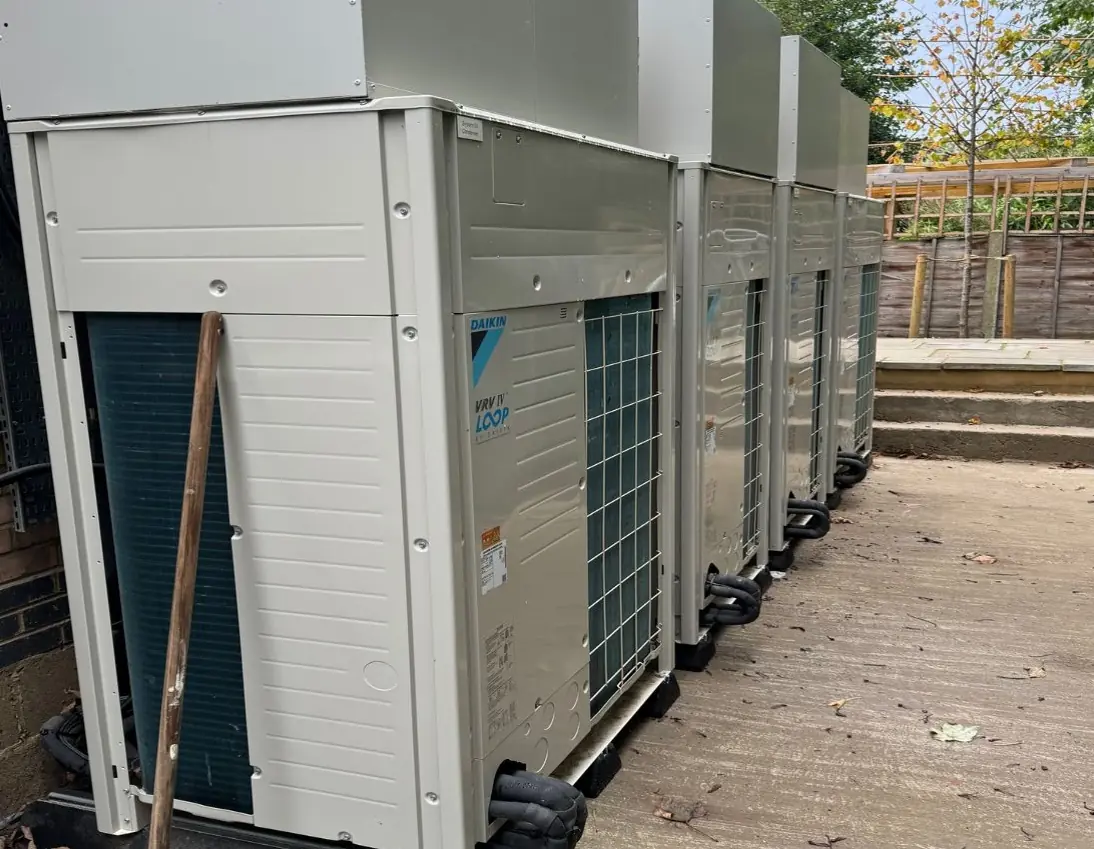 A row of four Daikin VRV outdoor units on a concrete plinth beside a brick wall, with insulated refrigerant pipework