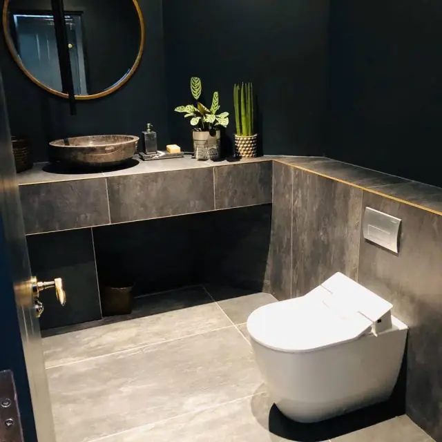 Cifonelli cloakroom with dark walls, stone vessel basin, round brass mirror and wall-hung shower toilet