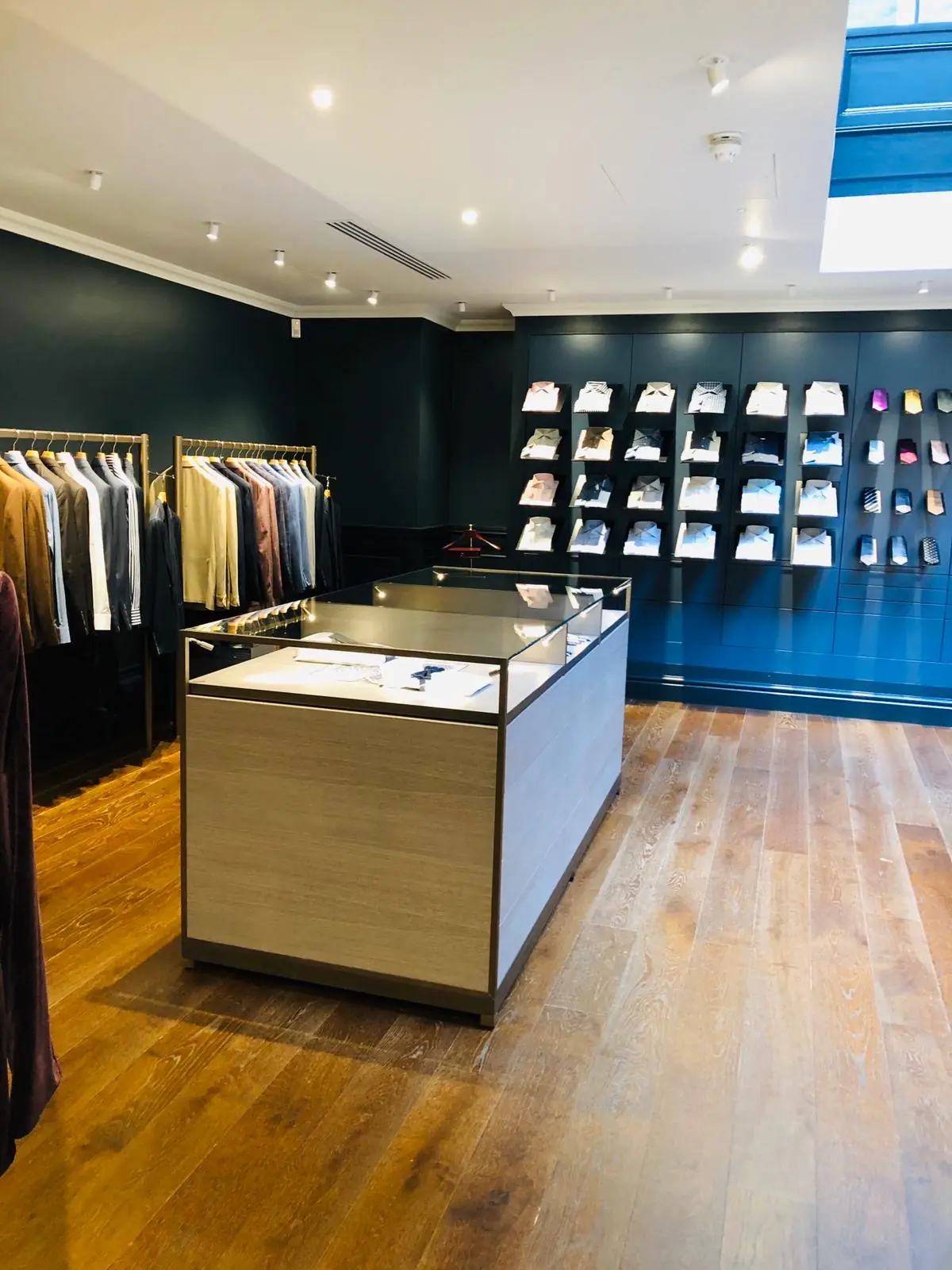 Cifonelli Mayfair shirt and tie wall, oak display counter and suit rails beneath a linear ceiling slot diffuser