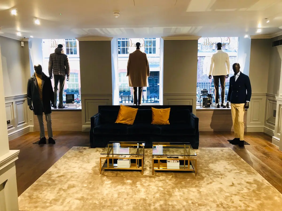 Cifonelli Mayfair showroom with navy velvet sofa, brass coffee tables and mannequins in the street-facing windows