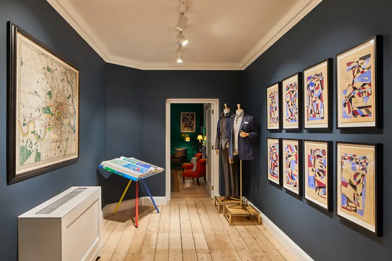 Navy corridor at Hackett Savile Row with track lighting, framed prints, tailored mannequins and a grilled heating unit