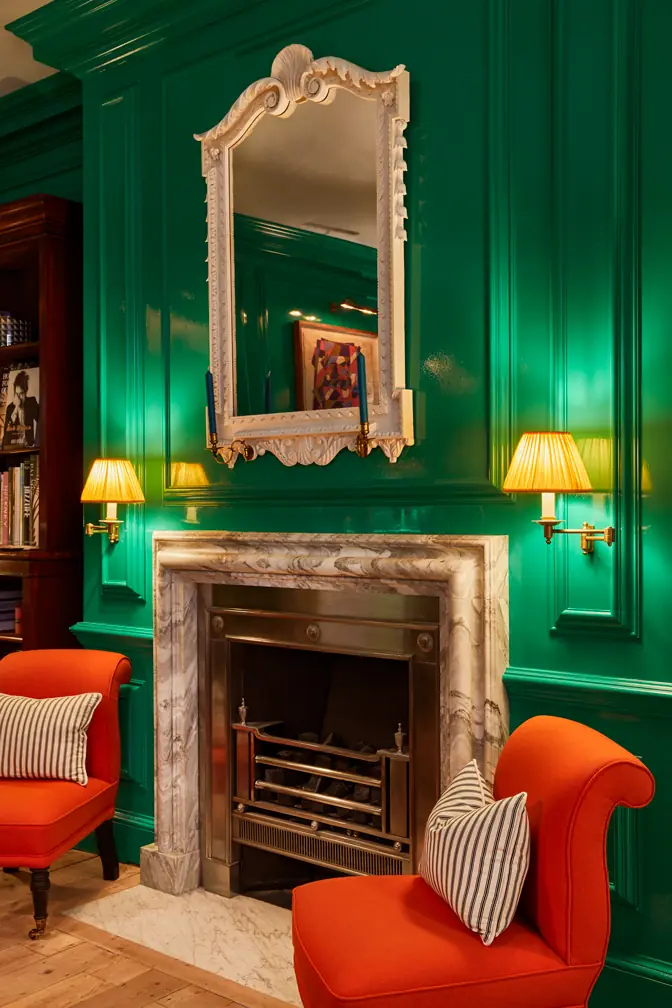 Marble fireplace in the emerald lacquered lounge at Hackett Savile Row, flanked by orange chairs and brass wall lights