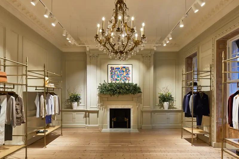 Grand panelled salon at Hackett Savile Row with gilt chandelier, track lighting, brass rails and garlanded fireplace