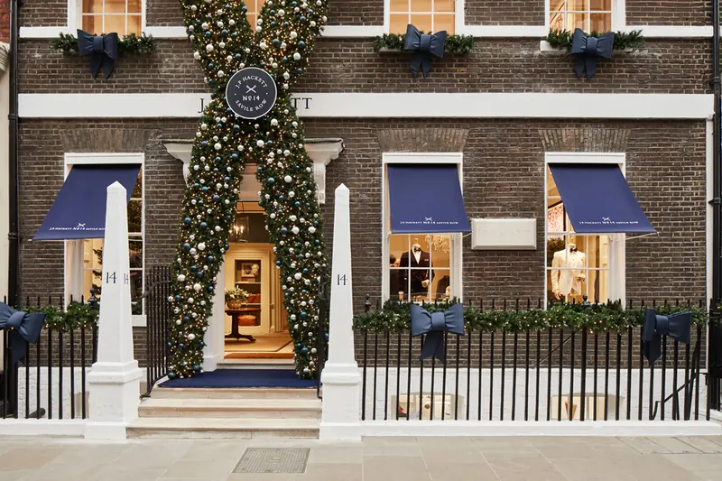 Hackett Savile Row shopfront at street level, with navy awnings, white obelisks and a festive scissor-shaped garland