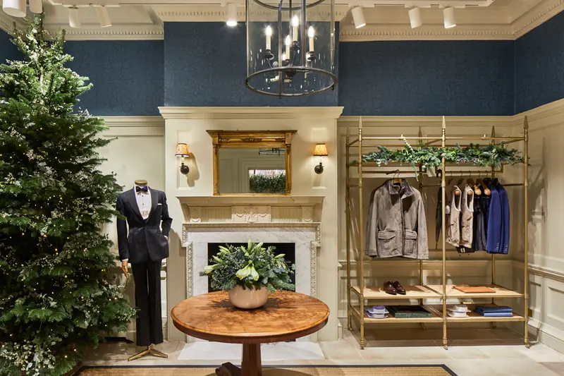 Hackett Savile Row panelled room with navy wallpaper, fireplace, lantern, tuxedo mannequin and brass clothing rail