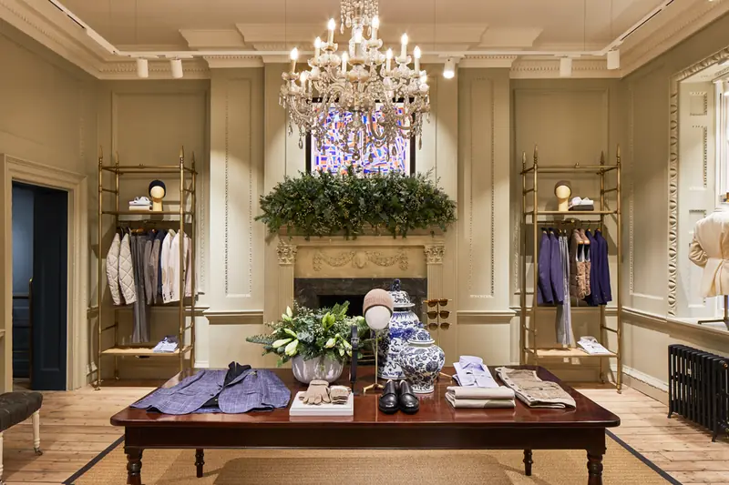 Hackett Savile Row showroom with crystal chandelier, garlanded fireplace, brass rails and central display table