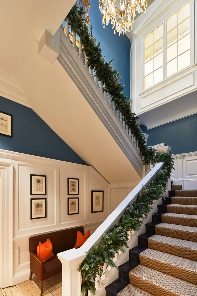 Georgian staircase at Hackett Savile Row with blue walls, white panelling, herringbone runner and festive garland