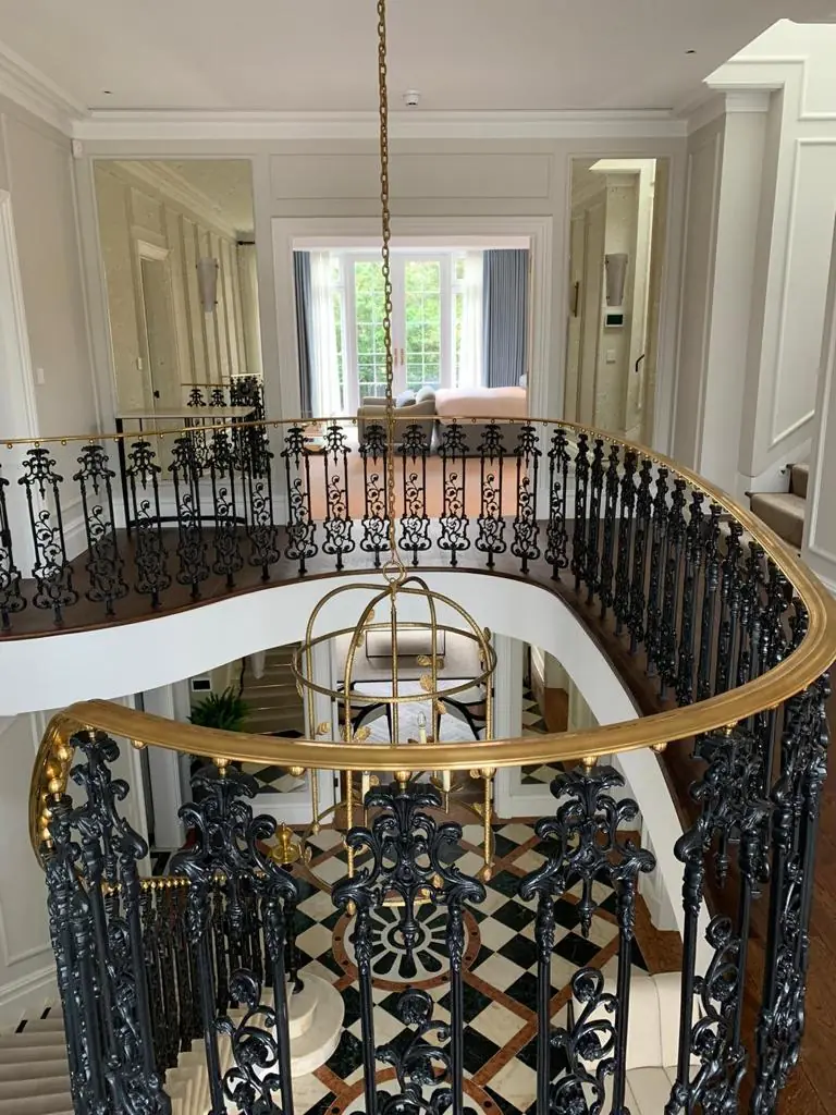 View down the Hampstead residence stairwell: wrought-iron balustrade, brass handrail, lantern pendant and marble floor