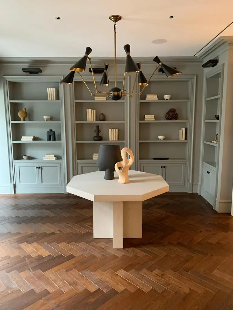 Hampstead residence library with grey-green built-in shelving, octagonal table and brass chandelier; linear slot diffuser at ceiling edge