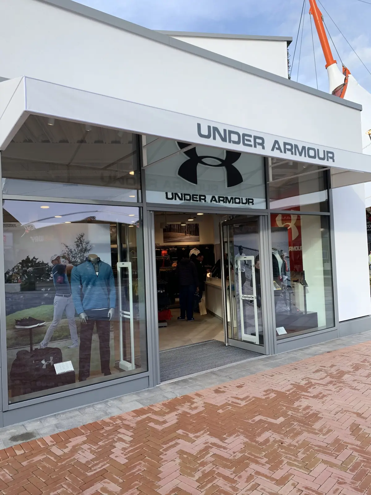 Under Armour shopfront at Ashford Designer Outlet, with white canopy signage, glazed entrance and herringbone paving