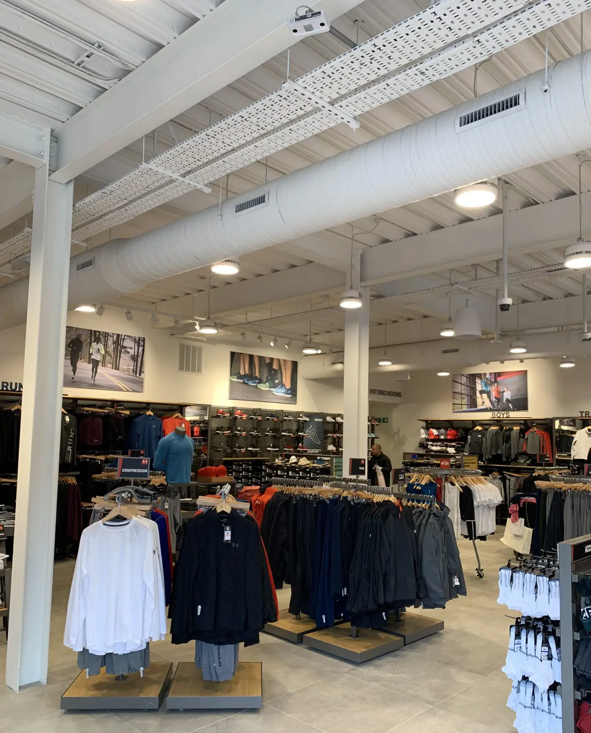 Under Armour Ashford store interior with exposed white spiral ductwork, supply grilles, cable tray and LED pendants