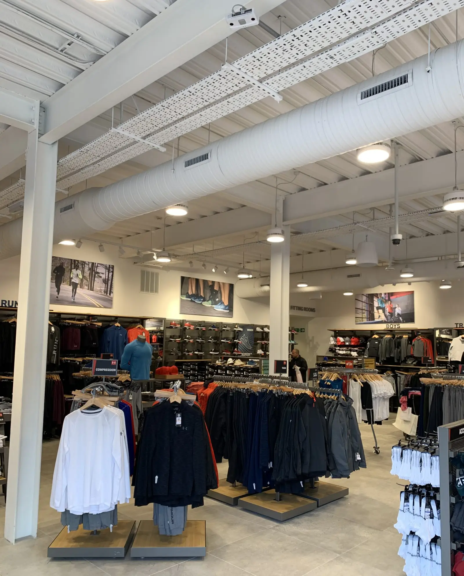 Under Armour Ashford store interior with exposed white spiral ductwork, supply grilles, cable tray and LED pendants
